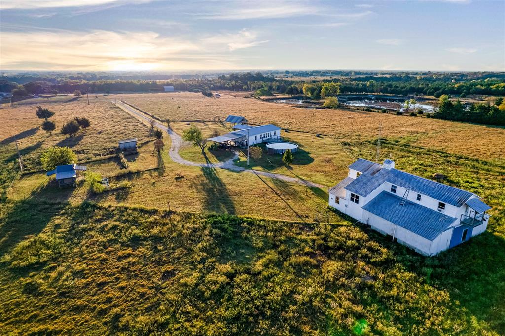 Expansive acreage featuring multiple structures, metal roofing, a long gravel driveway, and on-site water features