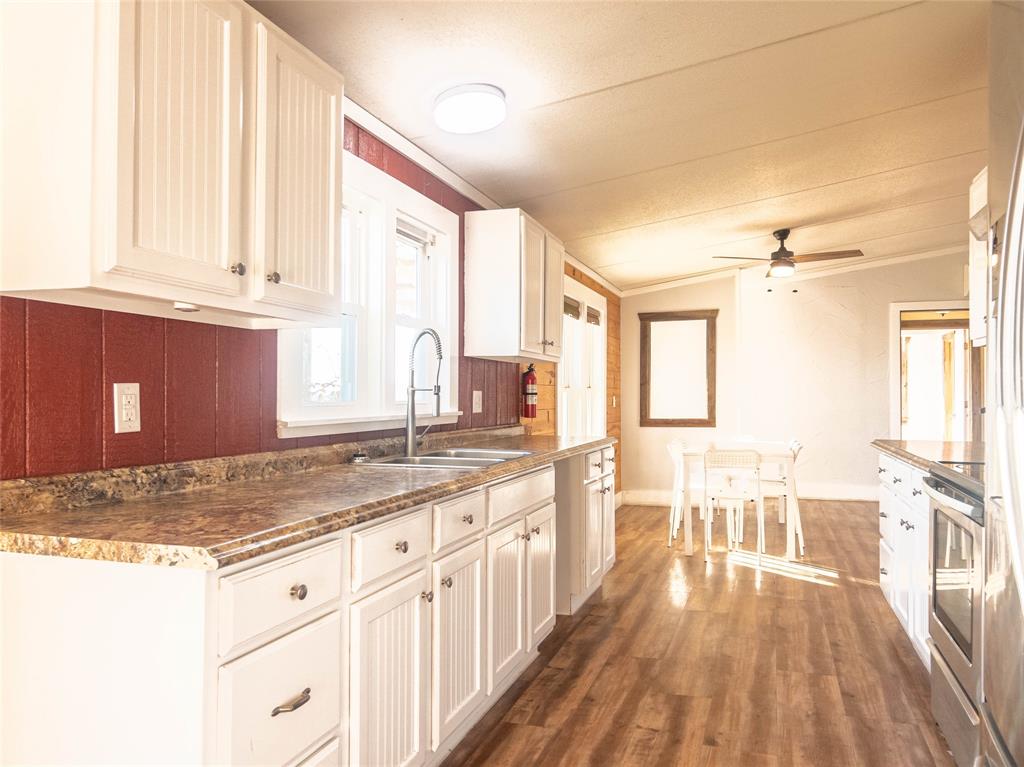 Kitchen featuring white cabinetry, stone-finish countertops, stainless steel sink with high-arc faucet, and wood-finish flooring