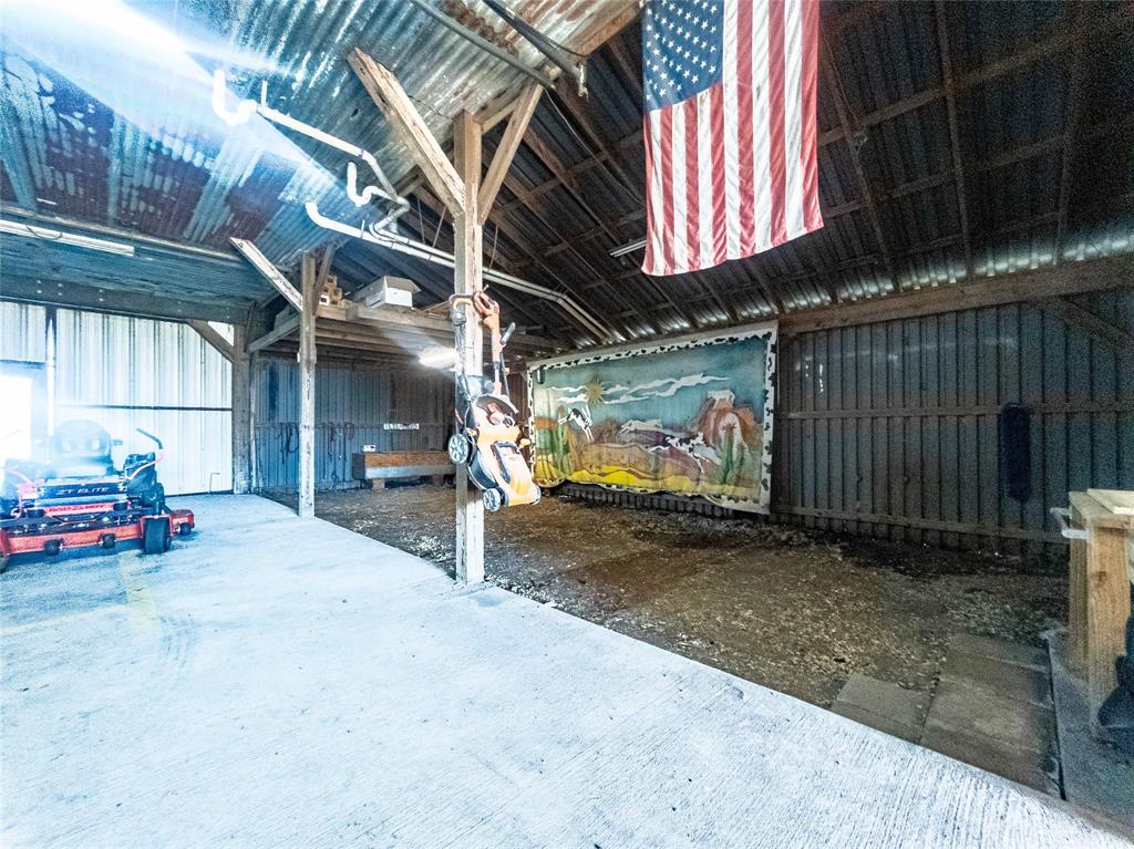 Open-bay structure featuring a corrugated metal roof, timber frame construction, concrete flooring, and vertical wall paneling