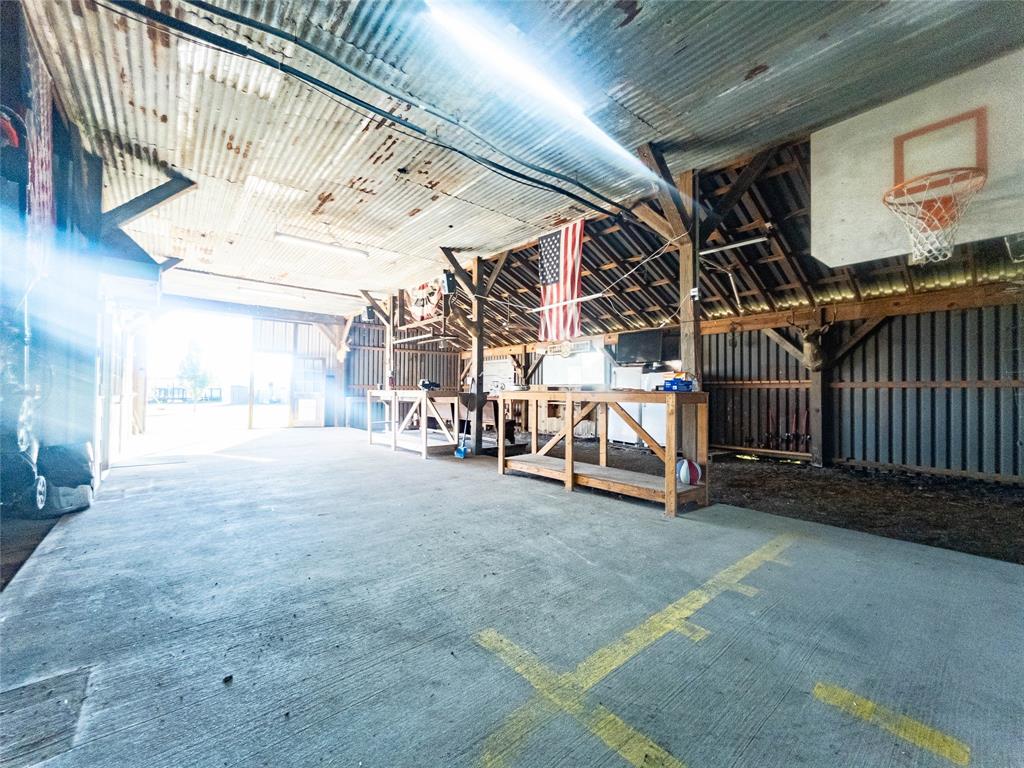 Expansive outbuilding featuring exposed timber framing, corrugated metal roofing, concrete flooring, and an integrated backboard