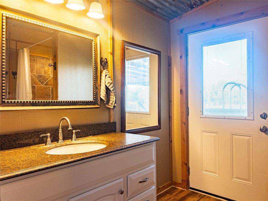 White cabinetry, stone-finish countertop with integrated sink, three-light vanity fixture, framed wall mirrors, and exterior door with inset glass