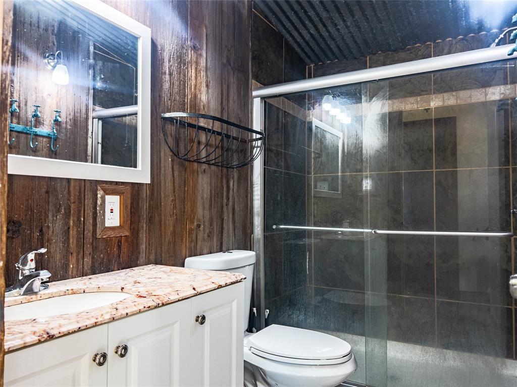 Bathroom featuring wood-paneled walls, a vanity with a light-toned stone countertop, a glass-enclosed shower with dark tile surround, and a metal corrugated ceiling