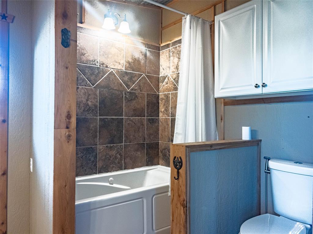 Bathtub surround with neutral-toned square tile, white wall-mounted cabinetry, integrated light fixture, and wood-trimmed partition wall