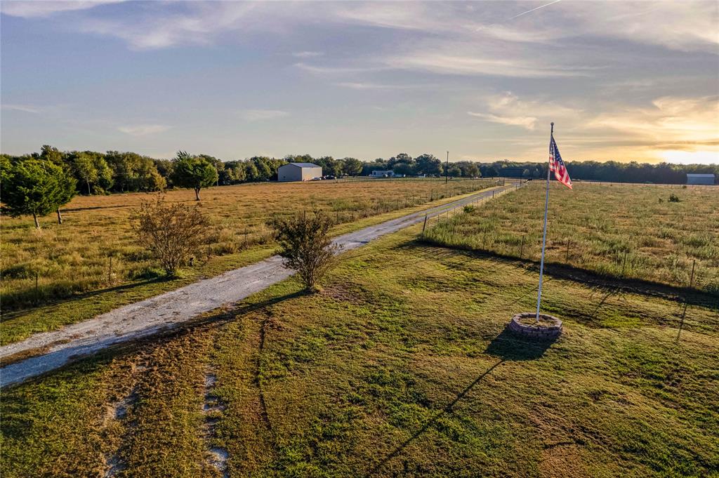 Expansive acreage featuring a gravel driveway, perimeter wire fencing, a flagpole with a masonry base, and a detached metal outbuilding