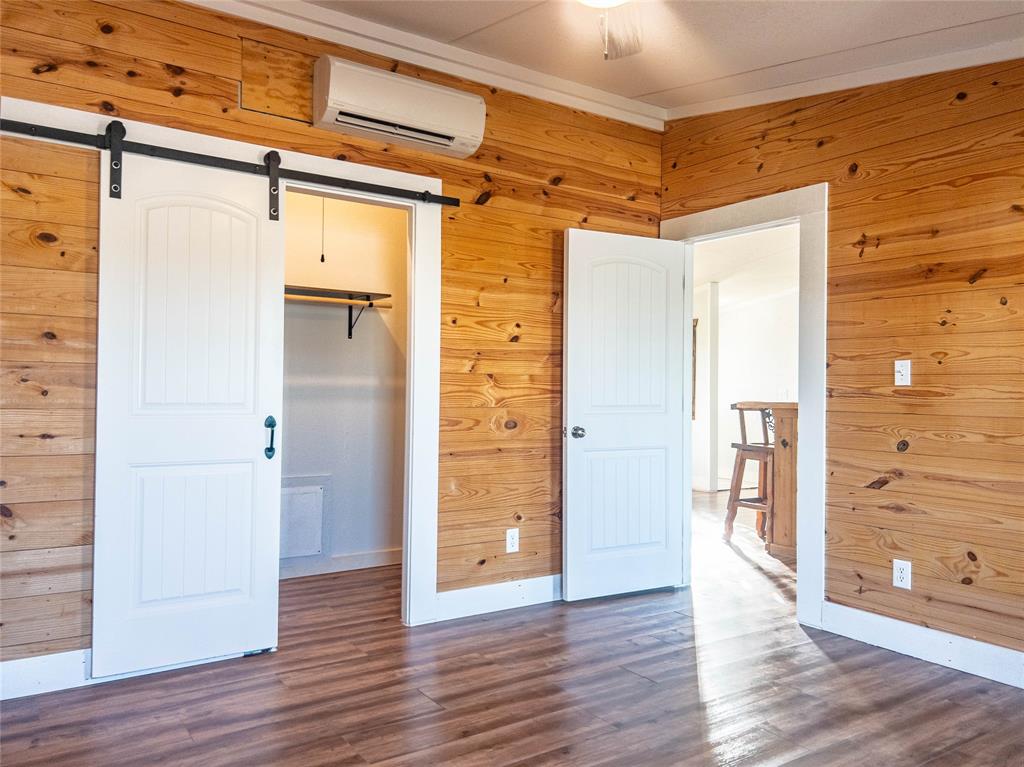Interior featuring horizontal wood wall paneling, wood-finish flooring, a sliding white barn door, and a wall-mounted climate control unit
