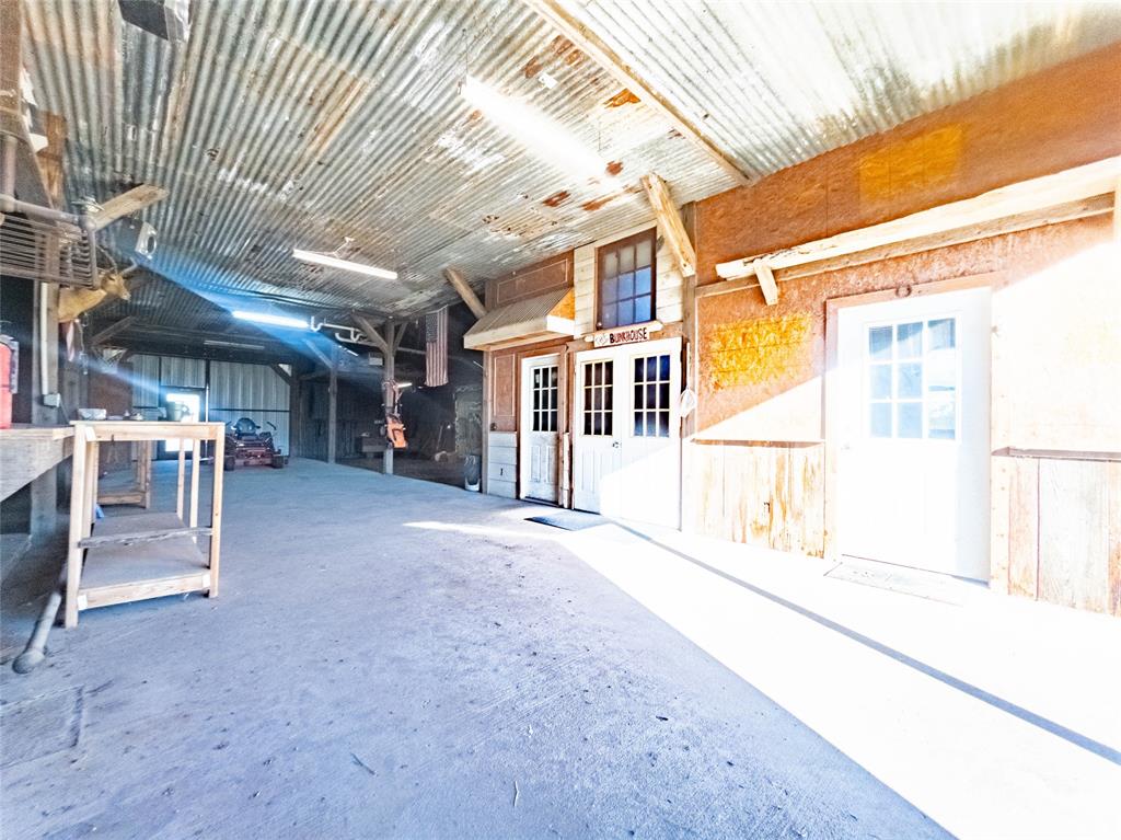 Interior workspace featuring a corrugated metal ceiling, exposed structural timber beams, concrete flooring, and multiple exterior-style entry doors