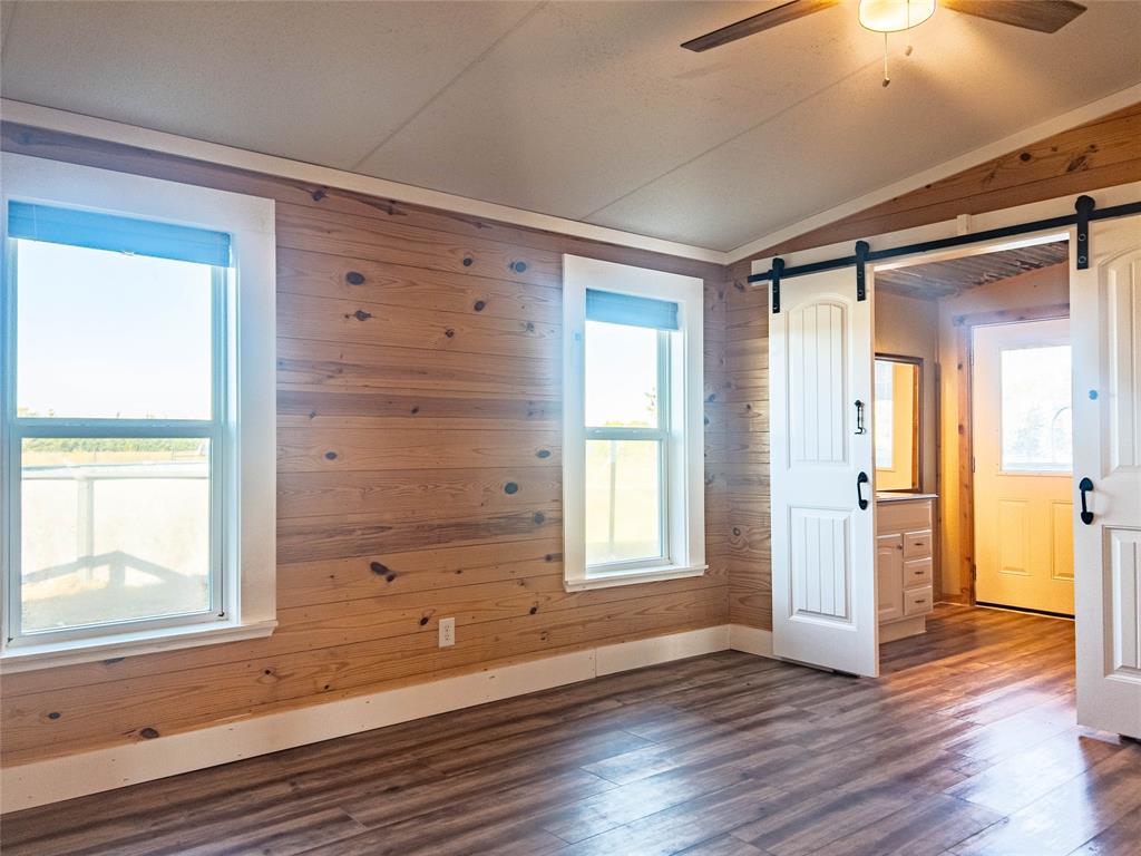 Interior featuring knotty pine wall paneling, wood-finish flooring, two sliding barn-style doors, and a ceiling fan with light fixture