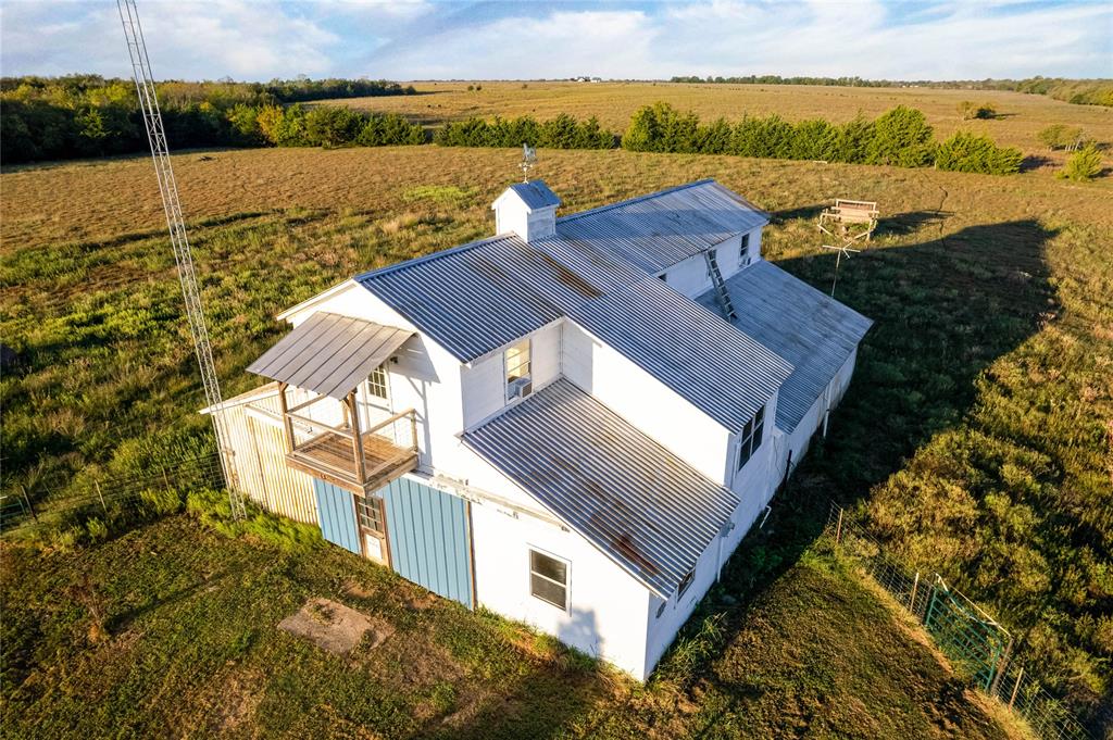 Aerial view of a structure featuring a metal roof, a cupola, a second-story wooden balcony, and white siding, set on an expansive parcel of land
