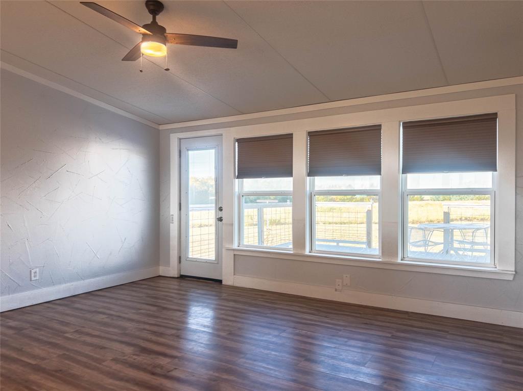 Room featuring wood-finish flooring, textured accent wall, ceiling fan with integrated lighting, and a bank of three large windows providing natural illumination