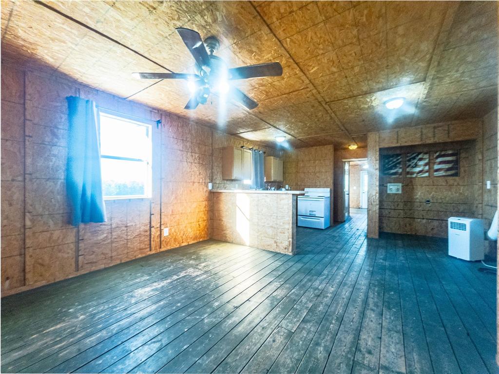 Open-concept interior featuring oriented strand board walls and ceiling, painted wood-plank flooring, a kitchen breakfast bar, and a ceiling fan with integrated lighting