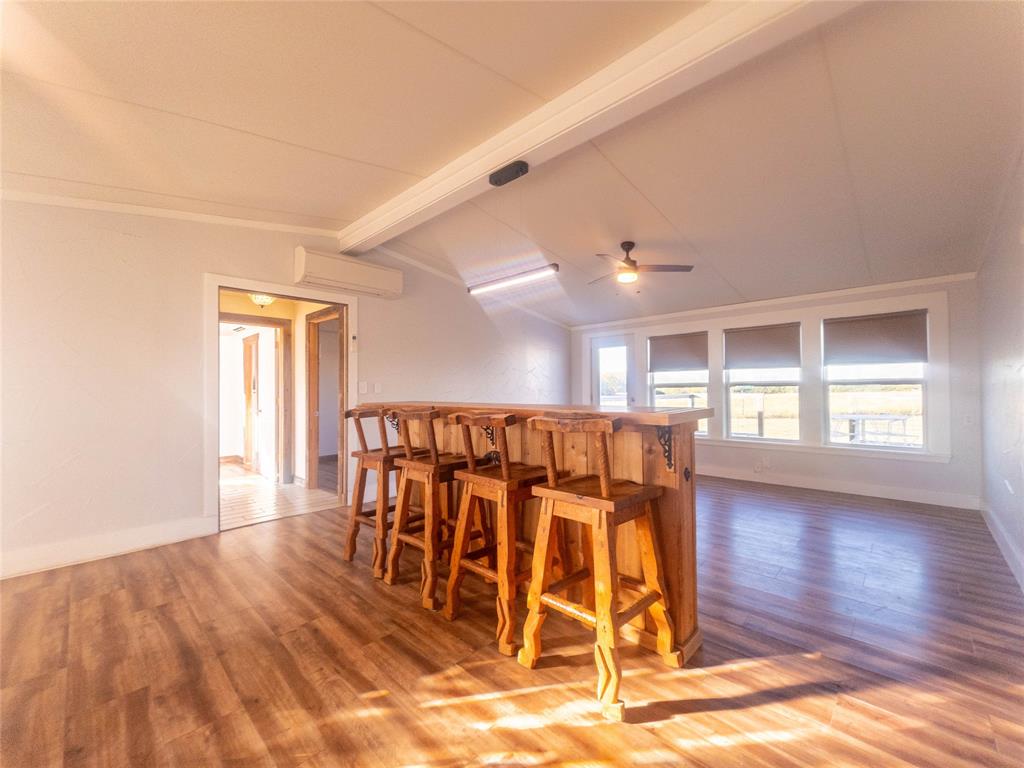Interior space featuring wood-finish flooring, vaulted ceilings, a built-in wood bar, a ceiling fan, and large windows with integrated blinds