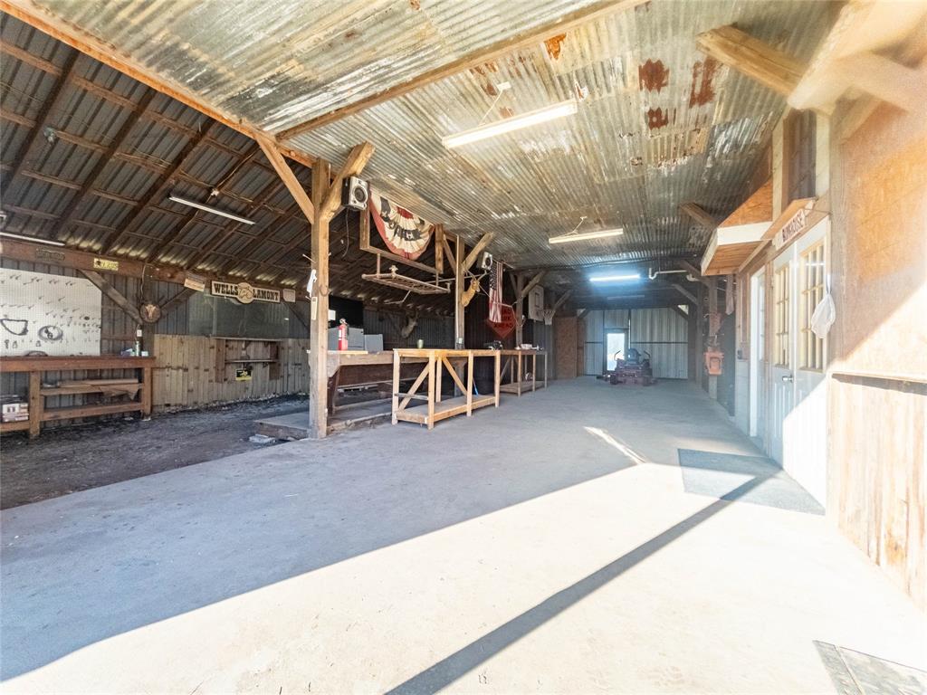 Enclosed barn structure featuring a concrete floor, corrugated metal ceiling, exposed timber post-and-beam construction, and multiple built-in wooden workbenches