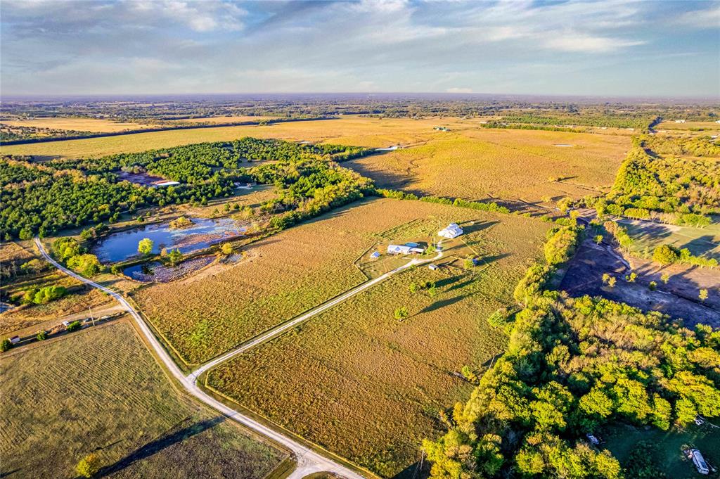 Aerial acreage featuring expansive pasture land, wooded perimeter, private pond, and gravel driveway access Aerial acreage featuring expansive pasture land, wooded perimeter, private pond, and gravel driveway access