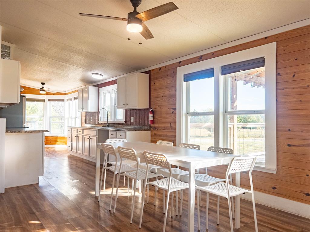 Kitchen featuring horizontal wood-paneled walls, wood-finish flooring, white cabinetry, solid-surface countertops, and a ceiling fan with integrated lighting
