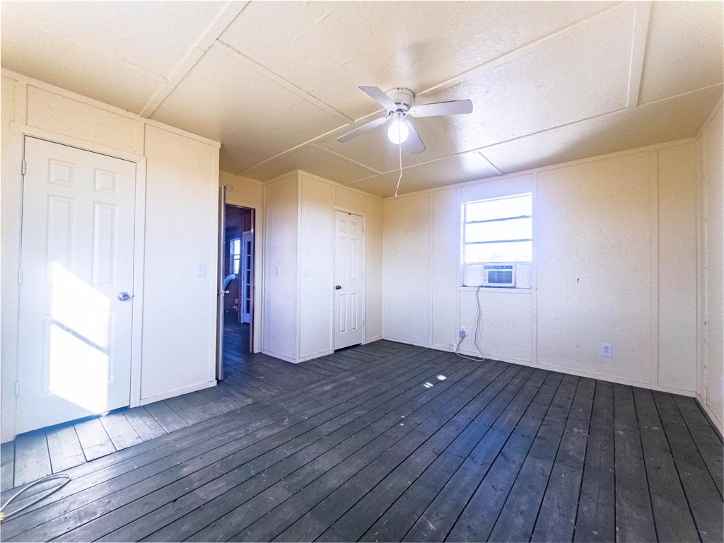 Interior space featuring dark-finish plank flooring, paneled walls, a ceiling fan with integrated lighting, and two interior doors