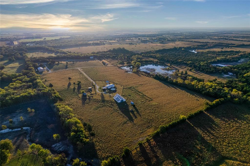 Aerial perspective of expansive acreage featuring open pasture land, established tree lines, multiple outbuildings, and a private pond