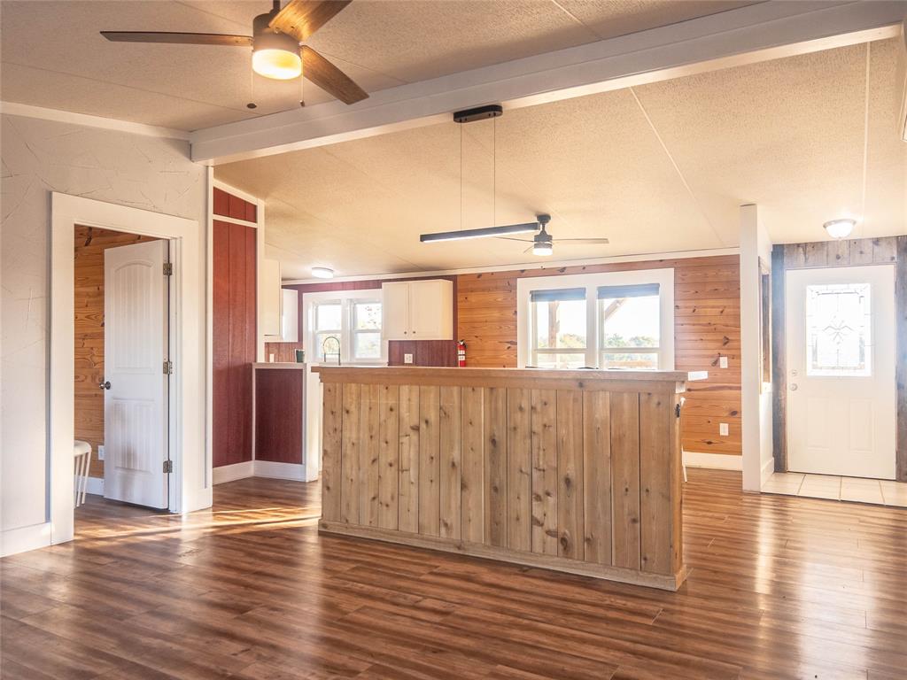 Wood-finish flooring, wood-paneled walls, built-in wooden bar, ceiling fans, and a white six-panel door with glass insert