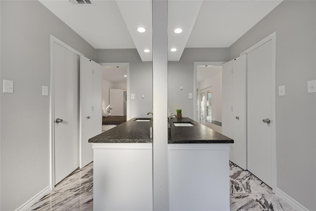 Dual vanity featuring dark stone countertops, undermount sinks, white cabinetry, recessed ceiling lighting, and patterned stone flooring