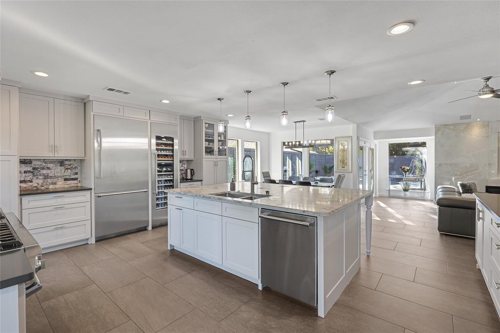 Kitchen featuring custom white cabinetry, a center island with a stone countertop, stainless steel appliances, a built-in wine cooler, and tile flooring