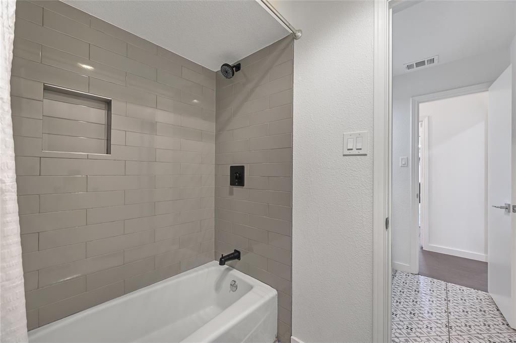 Shower featuring grey subway tile surround, built-in recessed wall niche, and matte black fixtures, paired with patterned tile flooring