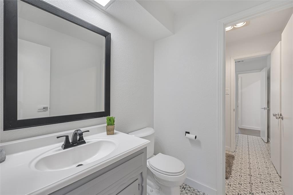 Bathroom featuring a gray vanity with an integrated basin, matte black faucet, framed mirror, and decorative patterned tile flooring