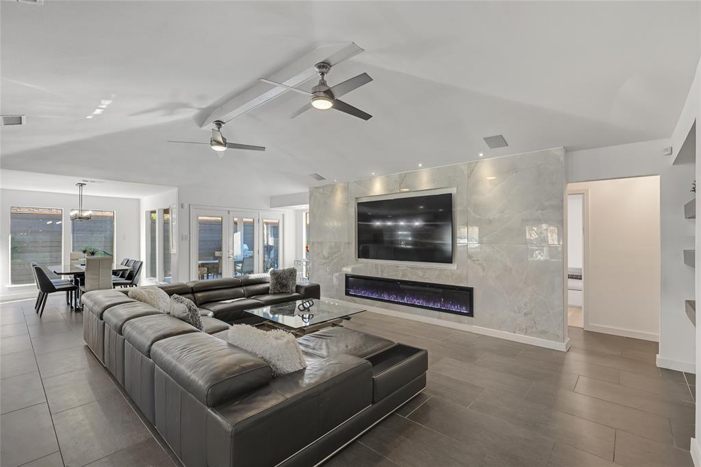 Vaulted ceilings featuring dual ceiling fans, large-format tile flooring, and a floor-to-ceiling stone-surround wall with a linear electric fireplace