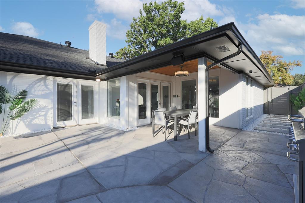 Covered rear patio featuring a flagstone-patterned concrete surface, recessed lighting, exposed wood-finish ceiling, and painted brick exterior