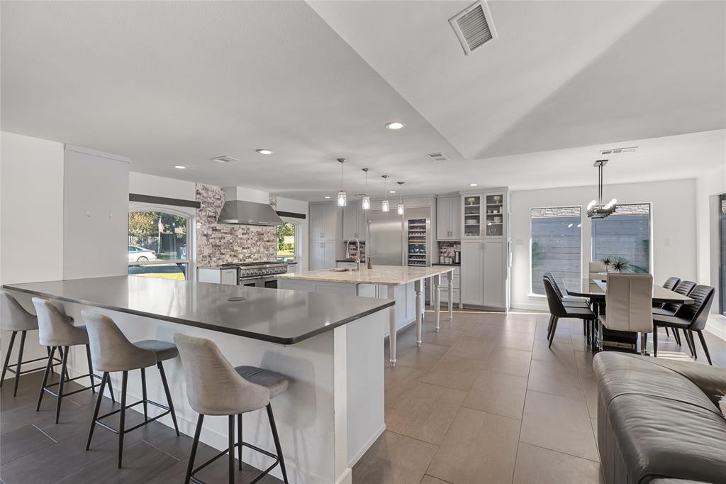 Kitchen featuring a large central island with light-toned stone countertop, expansive breakfast bar, stainless steel professional-grade range, decorative stone backsplash, and neutral tile flooring