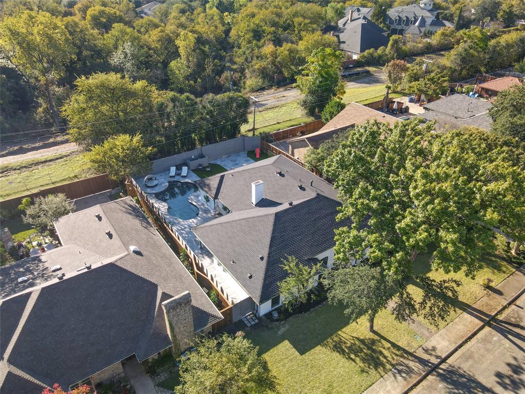 Aerial perspective of a multi-slope roof structure featuring a chimney, a rear pool, hardscaped patio, and surrounding mature trees