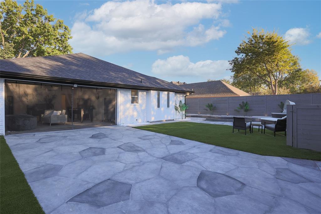 Backyard featuring a stamped concrete patio, synthetic turf lawn, white-painted brick exterior, and full-height perimeter wood fencing