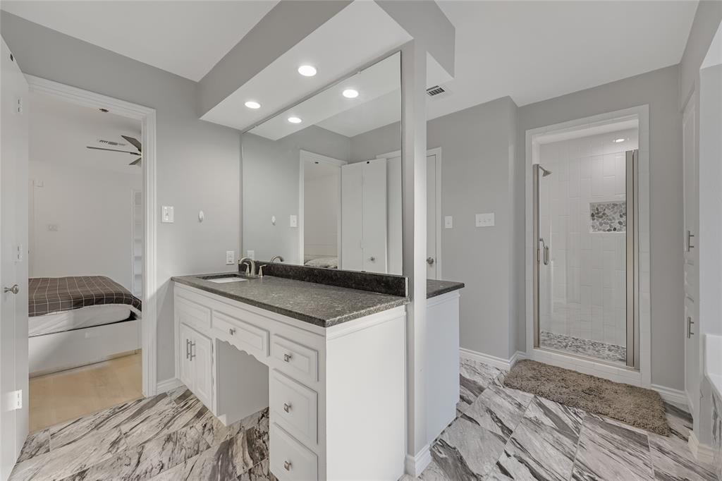 Vanity featuring a dark countertop, integrated sink, and white cabinetry with brushed metal hardware, complemented by full-width vanity mirror, recessed lighting, and large-format patterned floor tile