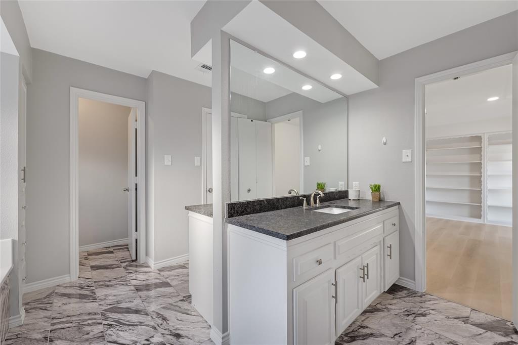 Vanity with white cabinetry, stone-finish countertop, undermount sink, and polished hardware, complemented by large-format patterned stone-finish flooring and recessed lighting
