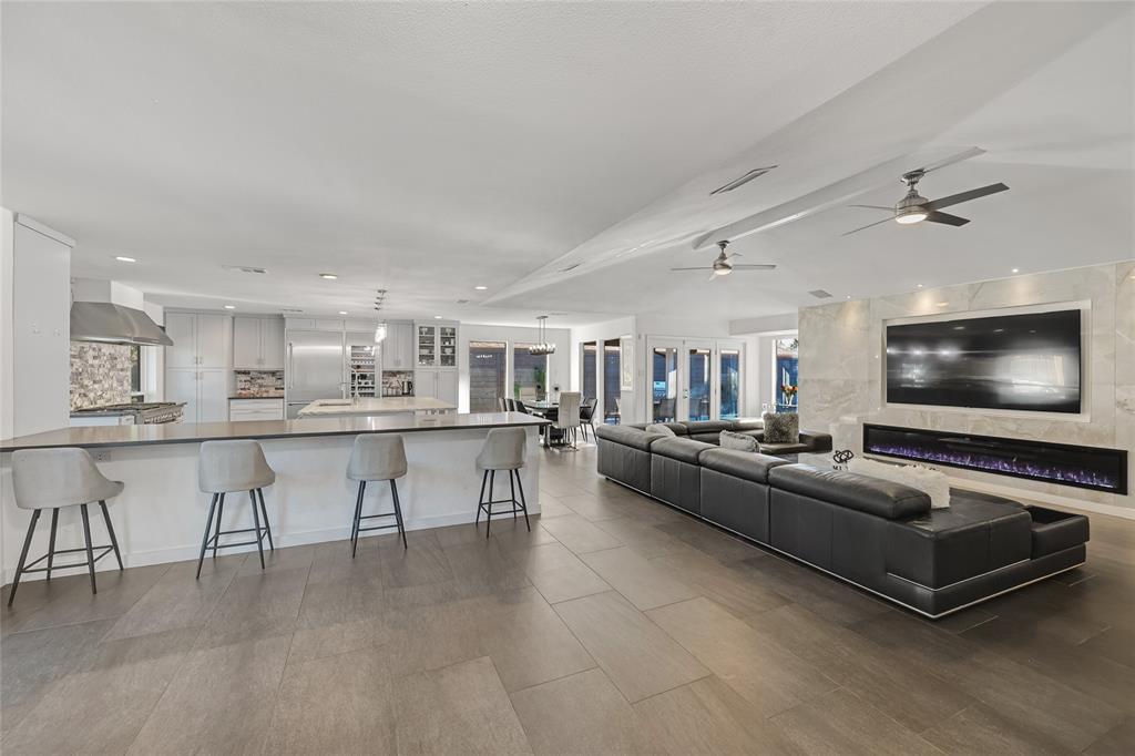 Open-concept interior featuring large-format tile flooring, a chef's kitchen with a stone-top center island, a linear electric fireplace set within a floor-to-ceiling stone surround, and dual ceiling fans