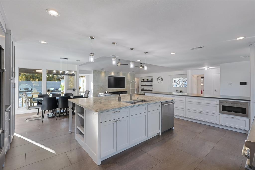 Kitchen featuring an oversized central island with stone-surface countertop, white shaker-style cabinetry, stainless steel dishwasher, tile flooring, and integrated pendant lighting
