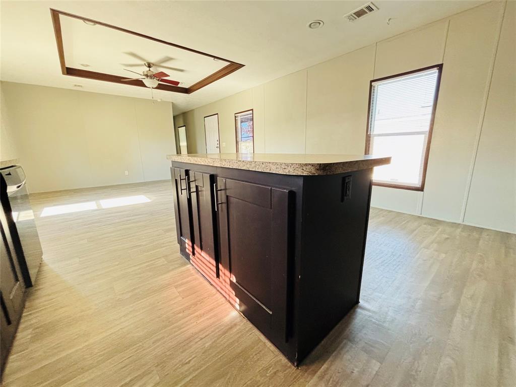 Kitchen island with dark cabinetry and speckled countertop, wood-finish flooring, tray ceiling with recessed lighting, and ceiling fan