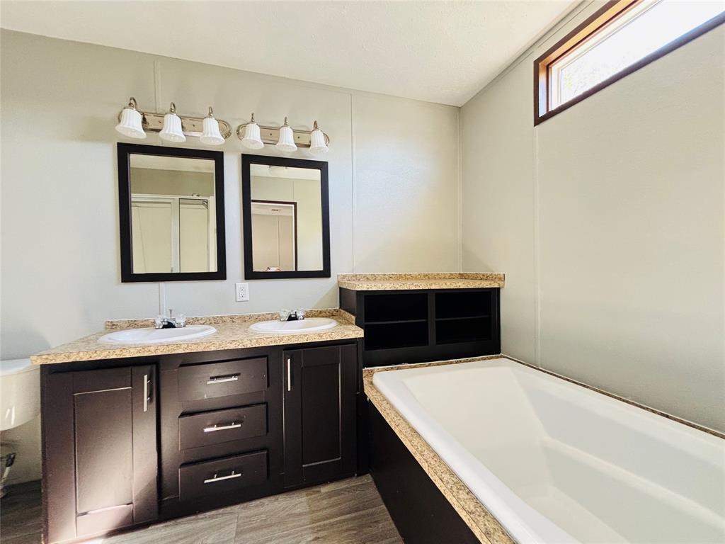 Dual vanity featuring dark cabinetry, stone-finish countertops, undermount sinks, and two wall-mounted mirrors, accompanied by a built-in soaking tub with a matching surround and horizontal clerestory window
