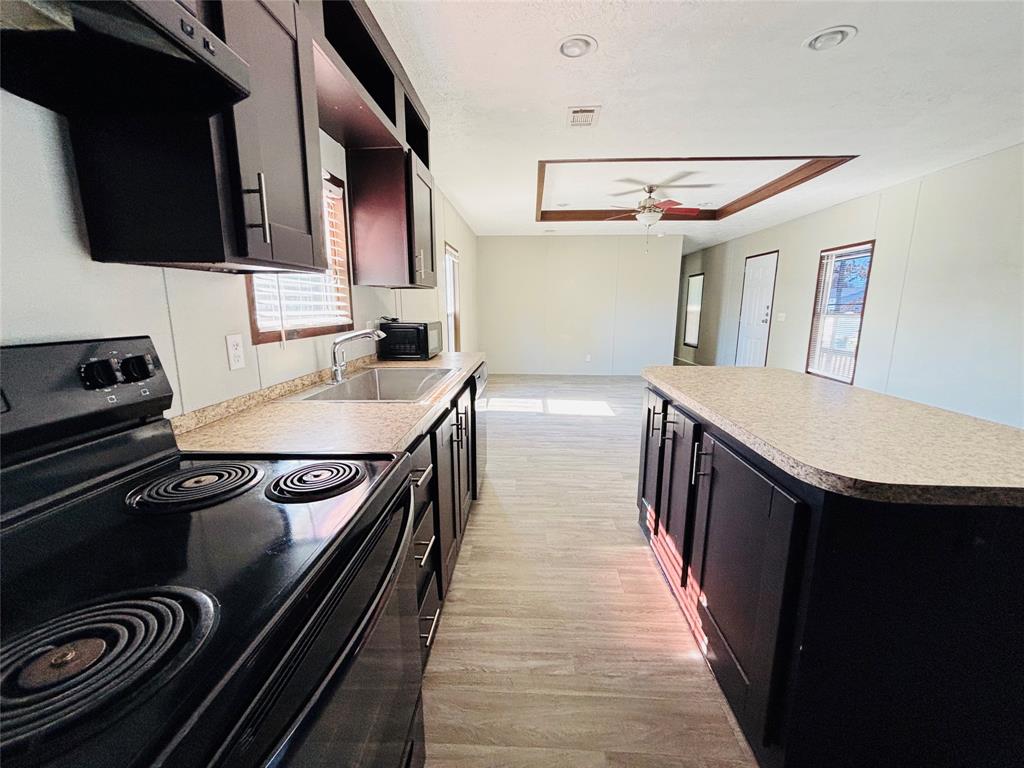 Kitchen featuring dark-finish cabinetry, a central island with a solid-surface countertop, stainless steel sink with a goose-neck faucet, black electric range, and wood-finish flooring