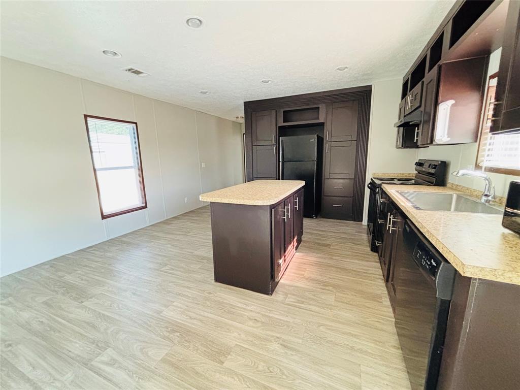 Kitchen featuring dark-toned cabinetry, a center island, stone-finish countertops, recessed lighting, and wood-finish flooring