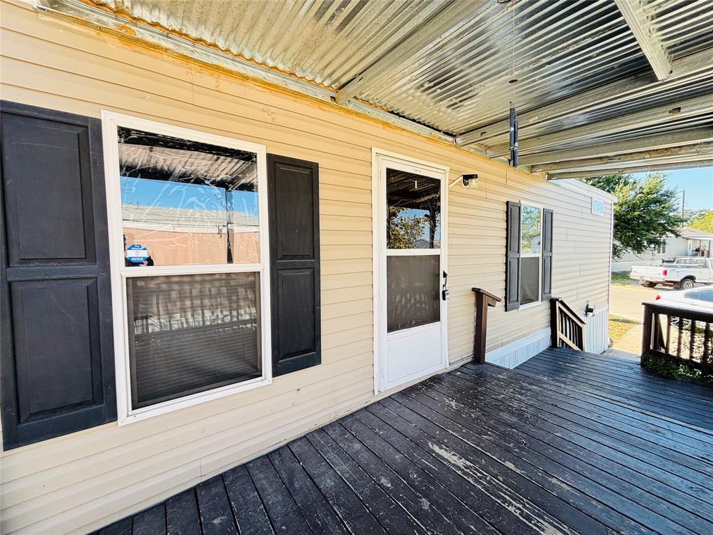 Exterior featuring horizontal siding, dark-toned shutters, a covered wooden deck, and a corrugated metal awning