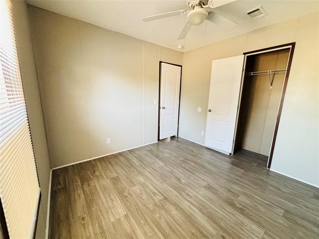 Room featuring wood-finish flooring, a ceiling fan with integrated lighting, neutral wall panels, and a closet with a built-in hanging rod