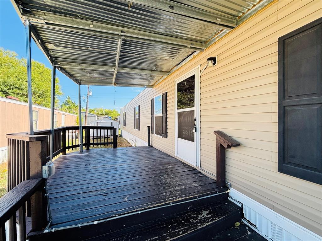 Exterior wood-plank deck featuring a metal-corrugated roof covering, dark-stained railing, and exterior shutters