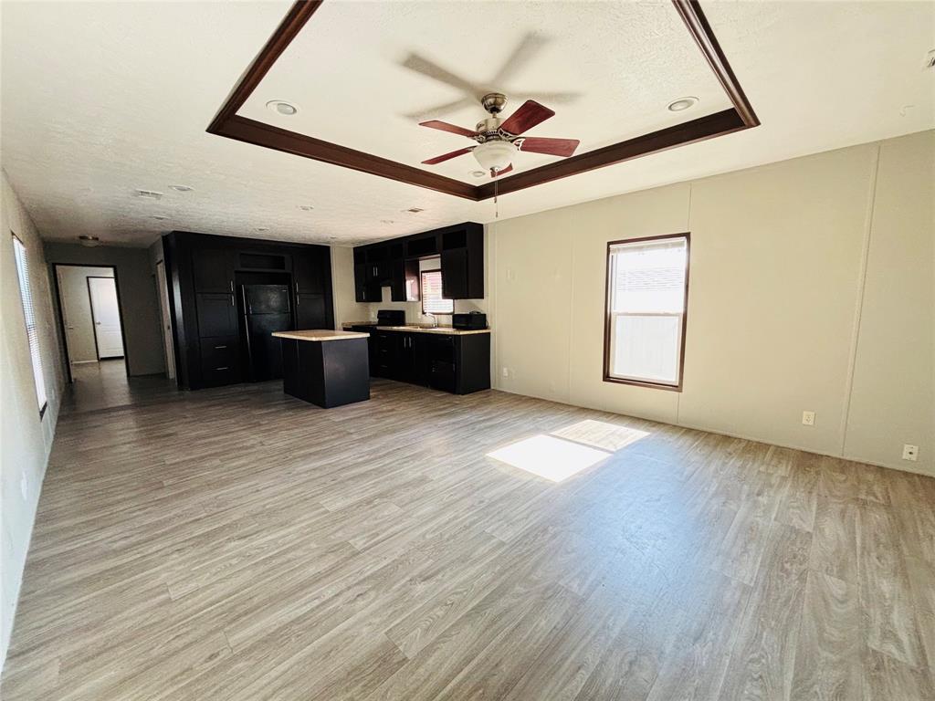 Open-concept interior featuring wood-finish flooring, tray ceiling with recessed lighting, and a kitchen equipped with dark cabinetry and a central island