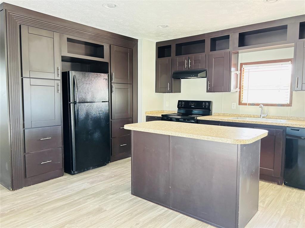 Kitchen featuring floor-to-ceiling dark wood cabinetry, a central island with a solid surface countertop, wood-finish flooring, and integrated black appliances