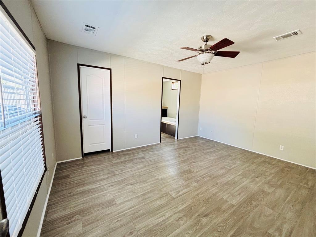Neutral-toned interior featuring wood-finish flooring, a ceiling fan with integrated lighting, and a white arched-panel door