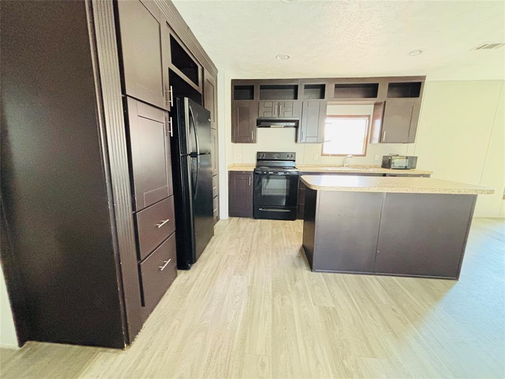 Kitchen featuring dark cabinetry, expansive center island with countertop seating, stone-finish countertops, recessed lighting, and wood-finish flooring