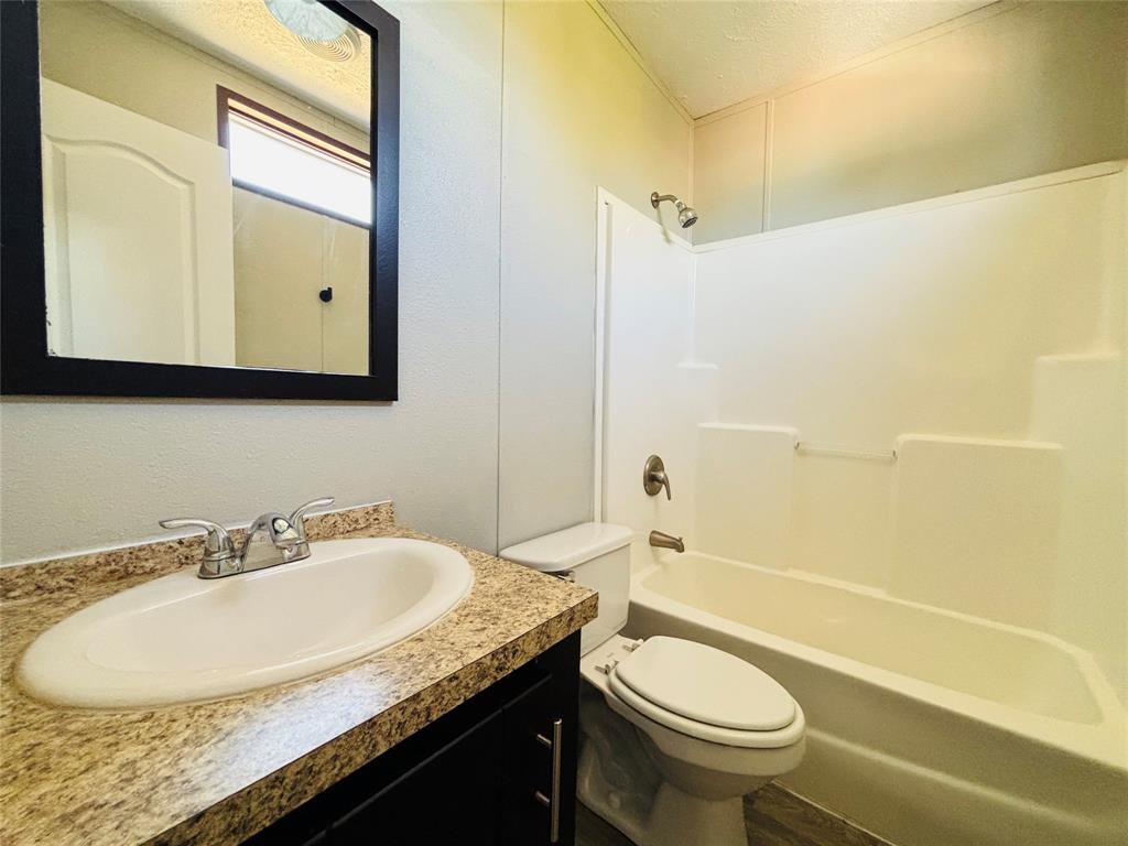 Bathroom featuring a dark wood-finish vanity with a stone-patterned countertop, an integrated oval sink, a wall-mounted mirror with a black frame, and a white tub-shower surround