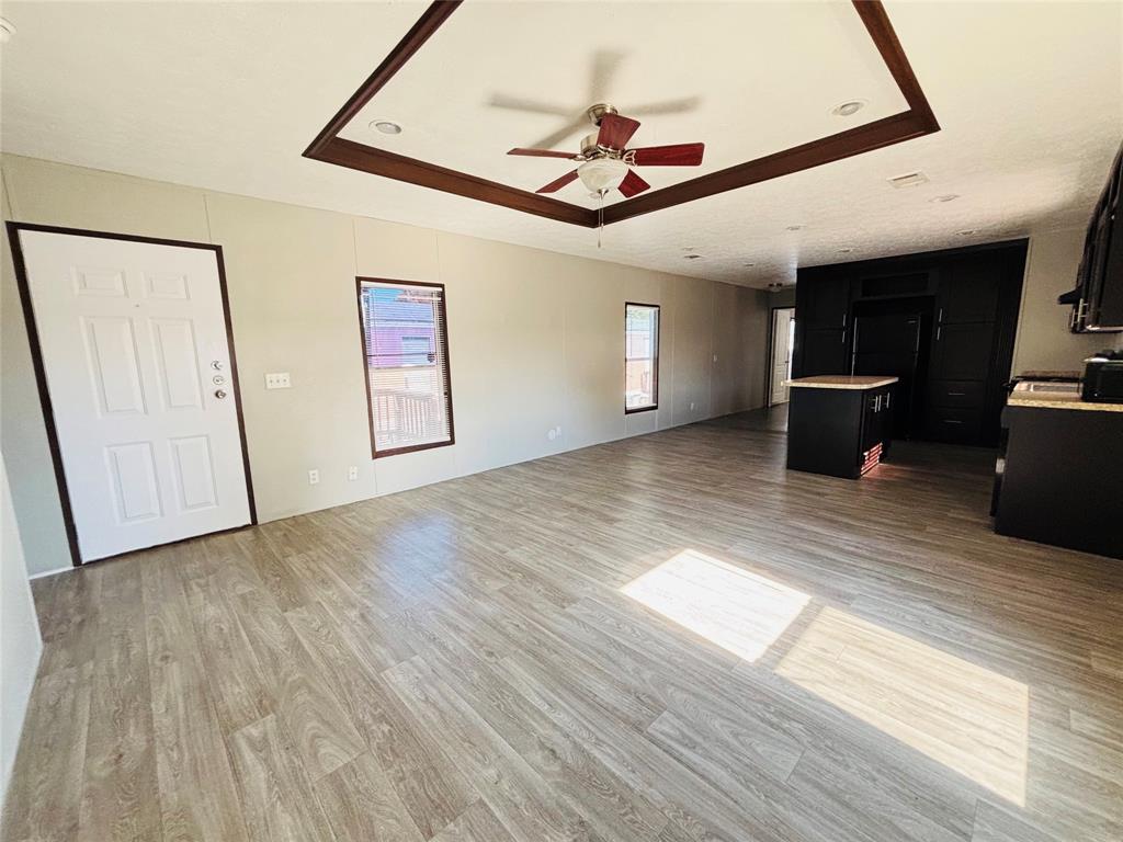 Tray ceiling with dark wood-finish trim, ceiling fan, wood-finish flooring, and black cabinetry with a central kitchen island