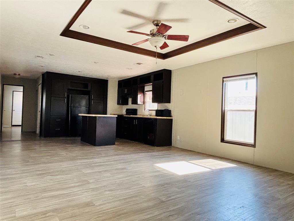 Open-concept kitchen featuring dark cabinetry, a central island, recessed lighting, wood-finish flooring, and a tray ceiling with a built-in ceiling fan