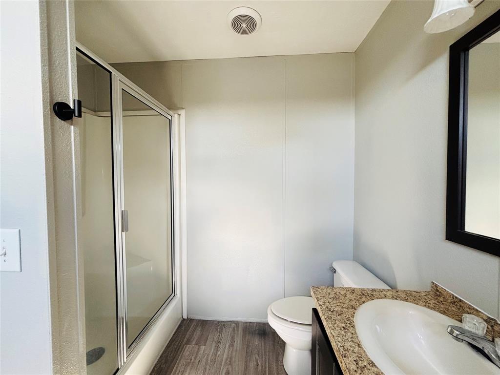 Bathroom featuring a glass-enclosed shower, stone-finish countertop with an integrated basin, wood-finish flooring, and a framed vanity mirror