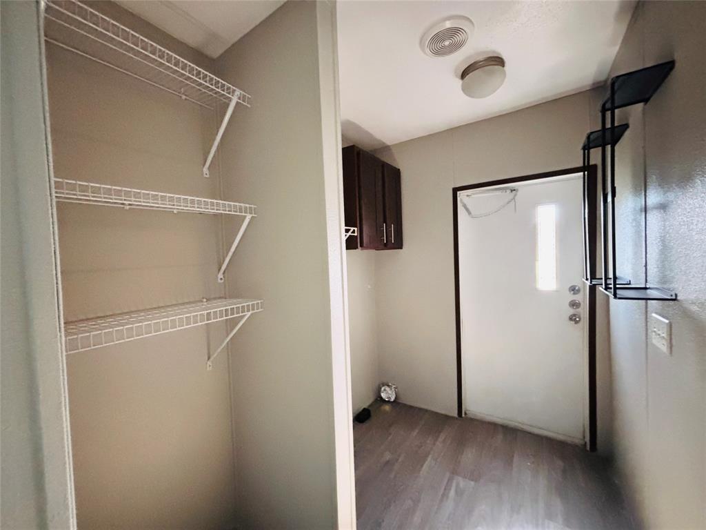 Utility area featuring wood-finish flooring, white wire shelving, dark wood-tone upper cabinetry, and a flush-mount ceiling light fixture